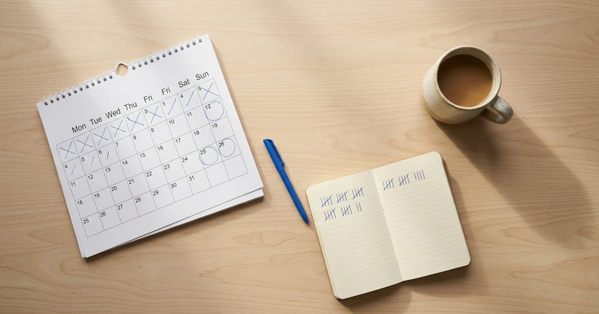 A paper calendar with circled dates, a notebook with tally marks and a cup of coffee on a desk